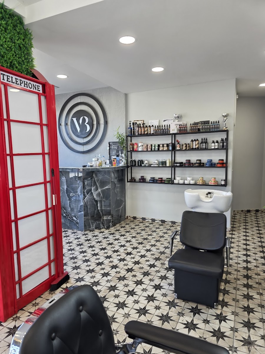 Το εσωτερικό του Voukou Barbershop με τον κοκκινο αγγλικο τηλεφωνικο θαλαμο, το κυκλικο εμβλημα VB και το αστερωτο δαπεδο